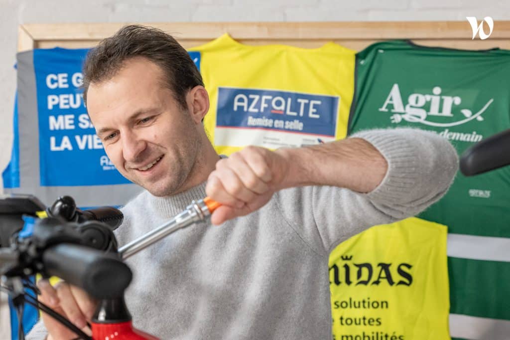 Homme réparant un vélo avec des maillots colorés en arrière-plan.